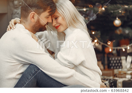 Beautiful couple sitting at home near christmas tree Beautiful couple sitting at home near christmas tree 63968842