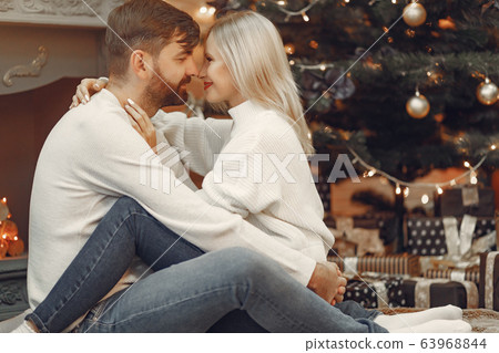 Beautiful couple sitting at home near christmas tree Beautiful couple sitting at home near christmas tree 63968844