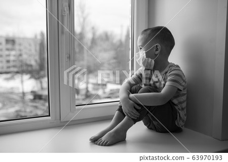 Sad little boy in medicine mask sitting near window and looking outside, quarantine at home, virus protection 63970193