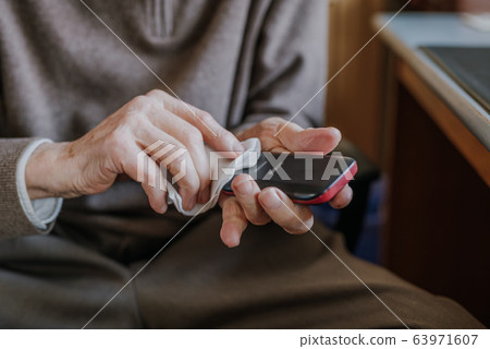 Old Man Cleaning phone to prevent Covid-19 infection 63971607