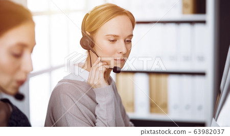 Businesswoman talking by headset in sunny office. Call center and diverse people group in business Businesswoman talking by headset in sunny office. Call center and diverse people group in business 63982037