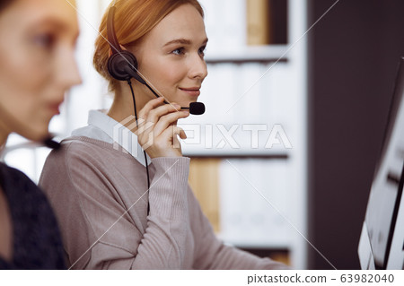 Businesswoman talking by headset in sunny office. Call center and diverse people group in business Businesswoman talking by headset in sunny office. Call center and diverse people group in business 63982040