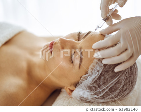 Beautician doing beauty procedure with syringe to face of young brunette woman. Cosmetic medicine and surgery, beauty injections Beautician doing beauty procedure with syringe to face of young brunette woman. Cosmetic medicine and surgery, beauty injections 63982140