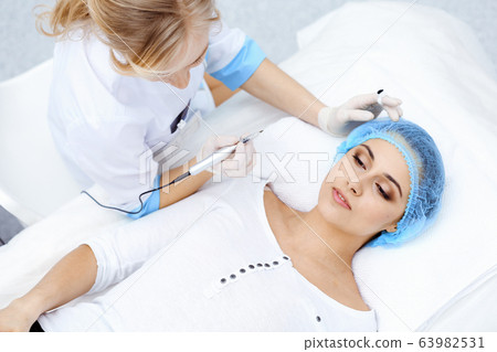 Professional beautician doing eyebrow tattoo at woman face. Permanent brow makeup in beauty salon, closeup. Cosmetology treatment Professional beautician doing eyebrow tattoo at woman face. Permanent brow makeup in beauty salon, closeup. Cosmetology treatment 63982531