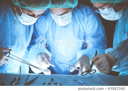 Group of surgeons wearing safety masks performing operation. Close-up of surgery tools. Medicine concept Group of surgeons wearing safety masks performing operation. Close-up of surgery tools. Medicine concept 63982560