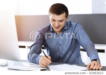 Businessman working with computer in modern sunny office. Headshot of male entrepreneur or company director at workplace. Business concept Businessman working with computer in modern sunny office. Headshot of male entrepreneur or company director at workplace. Business concept 63982621