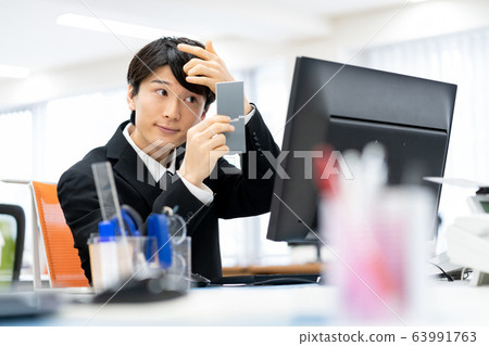 Young male employee checking his taste while looking in the mirror in the office 63991763
