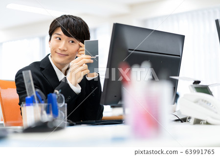 Young male employee checking his taste while looking in the mirror in the office 63991765