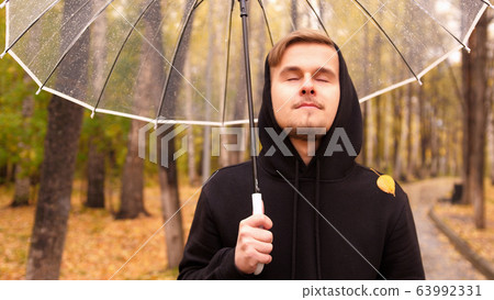 Portrait of a young man walking along the autumn park in a rainy day Portrait of a young man walking along the autumn park in a rainy day 63992331