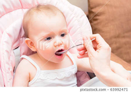 Feeding cute baby girl in pram with spoon Feeding cute baby girl in pram with spoon 63992471