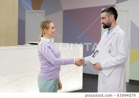 Pretty young blond woman in casualwear shaking hand of her doctor Pretty young blond woman in casualwear shaking hand of her doctor 63994879