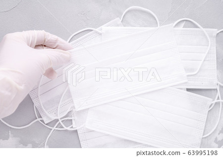 hand in glove takes a white medical mask on gray background hand in glove takes a white medical mask on gray background 63995198