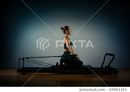 Young woman exercising on pilates reformer bed Stock Photo by