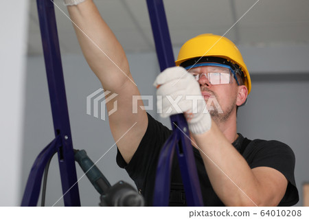 Builder holds metal equipment and looks at ceiling 64010208