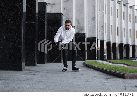 Young Professional videographer holding professional camera on 3-axis gimbal stabilizer. Pro equipment helps to make high quality video without shaking. Cameraman wearing white hoodie making a videos. 64011371