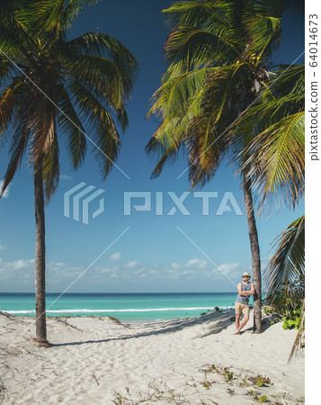younge man stay near the palm on the ocean beach of tropical island 64014673