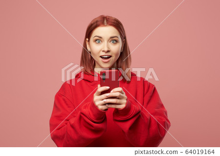 Happy ginger woman with phone in her hands standing in studio 64019164