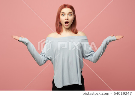 Surprised ginger woman with hands up in studio 64019247