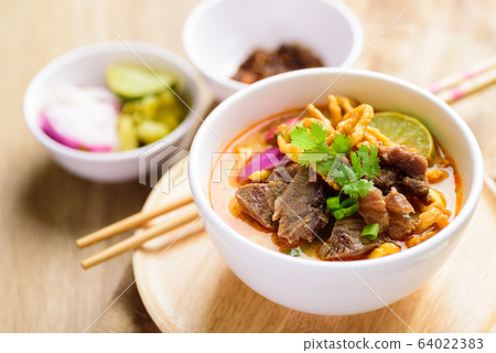 Northern Thai food (Khao Soi), spicy curry noodles soup with coconut milk and beef in a bowl on wooden table Northern Thai food (Khao Soi), spicy curry noodles soup with coconut milk and beef in a bowl on wooden table 64022383