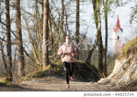 Corona virus, or Covid-19, is spreading all over the world. Portrait of caucasian sporty woman wearing a medical protection face mask while running in nature. Corona virus, or Covid-19, is spreading all over the world. Portrait of caucasian sporty woman wearing a medical protection face mask while running in nature. 64025724