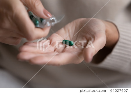 Middle aged woman pouring capsules pills out of plastic blister. Middle aged woman pouring capsules pills out of plastic blister. 64027407