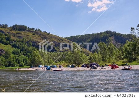 Tourist camp on the background of the river. Tents under the blue sky. Rafting on a mountain river. 64028012