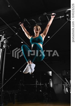 Woman working out in gym - pull ups. Image cross processed, contrasty, dark grainy image. Woman working out in gym - pull ups. Image cross processed, contrasty, dark grainy image. 64028226