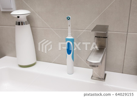 An electric toothbrush and an old toothbrush near the washbasin. An electric toothbrush and an old toothbrush near the washbasin. 64029155