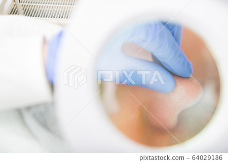 Beautician examines pores with magnifying mirror 64029186