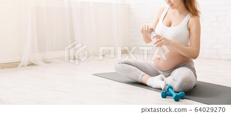 Young pregnant woman drinking water sitting in lotus position 64029270