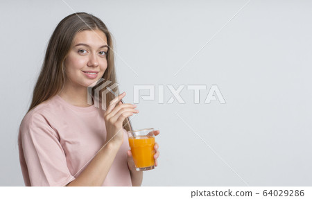 Young cheerful girl drinking orange juice with straw Young cheerful girl drinking orange juice with straw 64029286