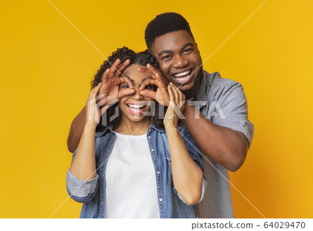 Cheerful Afro Boyfriend Making Funny Glasses To Laughing Girlfriend 64029470