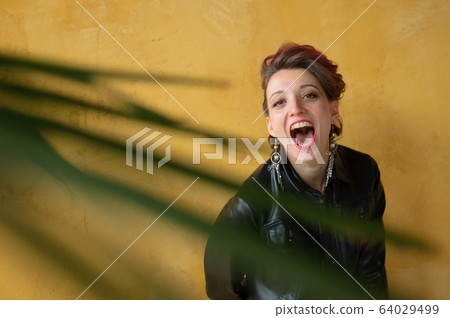 Glamorous lady in punk rock style party clothes with dark pink hair in casual dress, black leather jacket, and long earrings on yellow background Glamorous lady in punk rock style party clothes with dark pink hair in casual dress, black leather jacket, and long earrings on yellow background 64029499