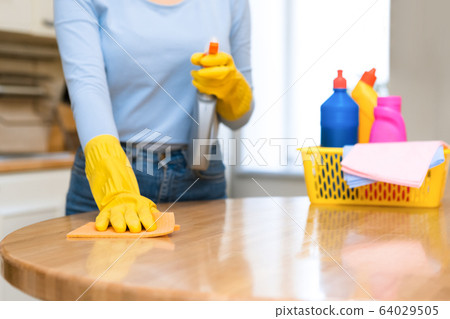 Young woman cleaning kitchen table using spray and rag Young woman cleaning kitchen table using spray and rag 64029505