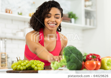 Happy young black woman preparing vegetable salad Happy young black woman preparing vegetable salad 64029626