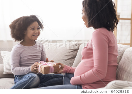 Little black daughter giving gift to her surprised pregnant mom 64029818