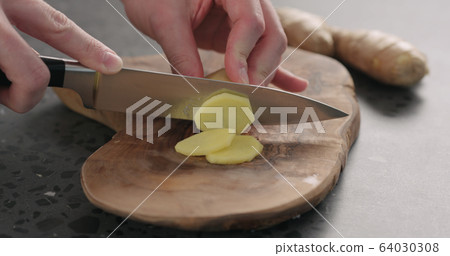 man hands slicing fresh ginger root with knife on olive wood board 64030308