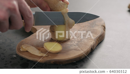 man hands peeling fresh ginger root with knife on olive wood board 64030312