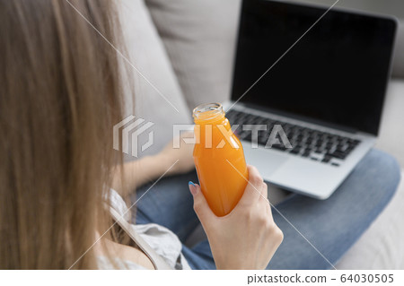Unrecognizable woman working on laptop and drinking detox orange juice Unrecognizable woman working on laptop and drinking detox orange juice 64030505