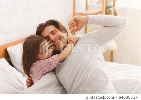 Adorable girl hugging her happy father after waking up Adorable girl hugging her happy father after waking up 64030517