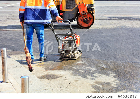 A road worker uses a gasoline vibratory compactor, 64030888