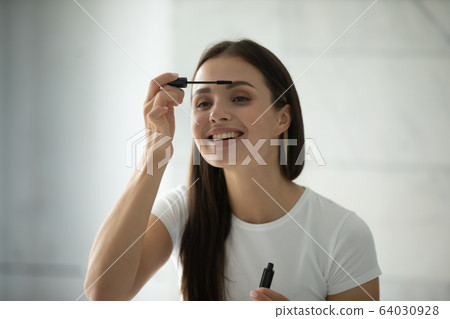 Young woman look in mirror paint eyelashes 64030928