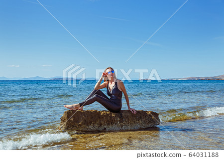 Young woman sits on a boulder in the sea. Young woman sits on a boulder in the sea. 64031188