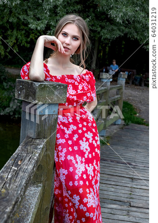 A beautiful young girl with perfect skin, with long hair in a red dress lies on a tree branch with a relaxed A beautiful young girl with perfect skin, with long hair in a red dress lies on a tree branch with a relaxed 64031219