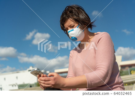 A woman in a mask on her face during quarantine from the coronavirus and from spring allergies, with a smartphone. A woman in a mask on her face during quarantine from the coronavirus and from spring allergies, with a smartphone. 64032465
