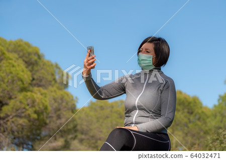 Girl in the period of coronavirus in a mask behind a phone on nature. Social isolation. 64032471