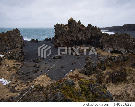 Rugged lava rocks on a black sandy beach Rugged lava rocks on a black sandy beach 64032628