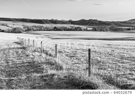 Hilly landscape illuminated by evening sunset. Green grass fields and hills on the horizont. Vivid spring rural countryside. Ralsko Mountain, Czech Republic Hilly landscape illuminated by evening sunset. Green grass fields and hills on the horizont. Vivid spring rural countryside. Ralsko Mountain, Czech Republic 64032679