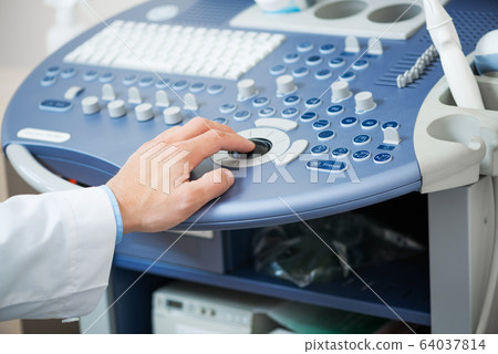 Sonographer using ultrasound machine at work. 64037814