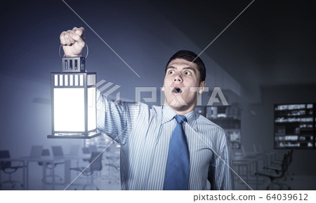 Horrified businessman holding glowing lantern Horrified businessman holding glowing lantern 64039612